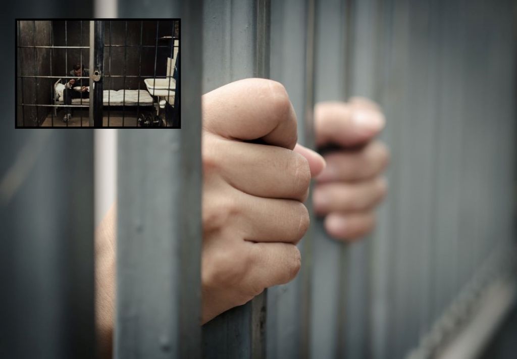 Hands gripping metal bars of a prison cell, with a person visible through the window in the background.