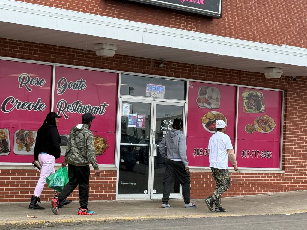 Exterior of Rose Creole Cajun Restaurant with people entering and exiting the establishment. The restaurant's name and logo are prominently displayed on the storefront.