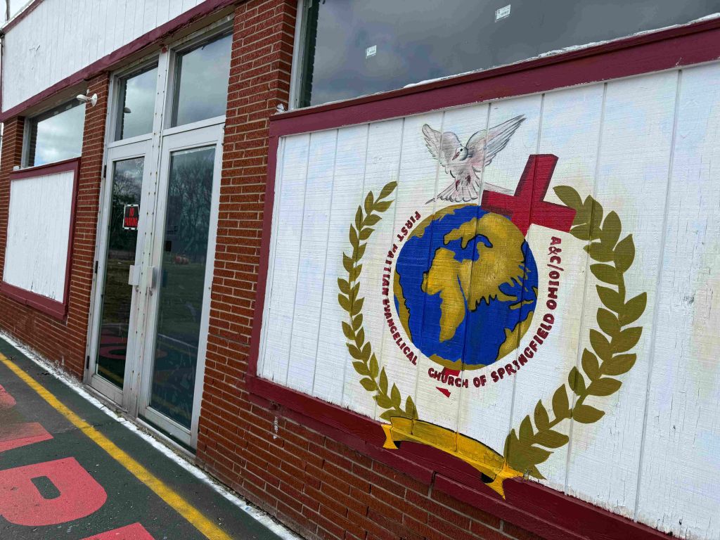 Exterior of a brick building with a mural depicting a globe, cross, and dove. The mural includes the text "Church of Pentecost".
