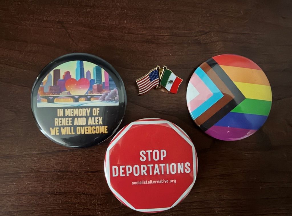 A collection of political and social justice buttons and pins, including a "Stop Deportations" sign, a rainbow-colored circular design, and a memorial message "In Memory of Renee and Alex We Will Overcome".