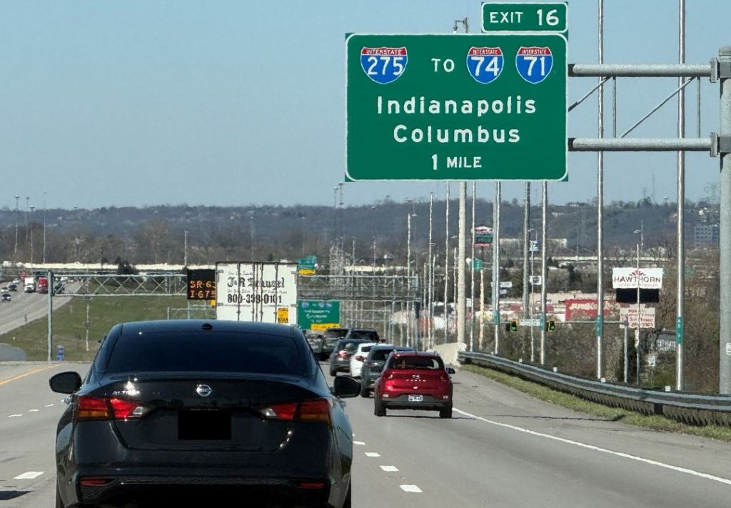 Highway sign indicating directions to Indianapolis and Columbus, 1 mile ahead. Cars on the highway.