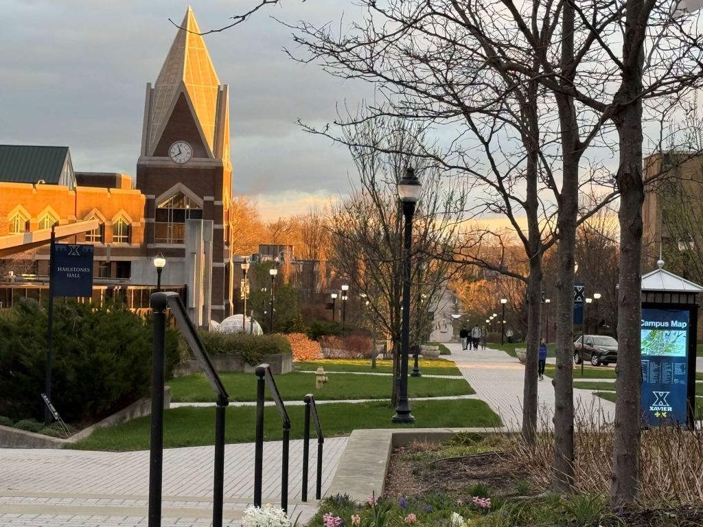 A scenic campus view with a tall clock tower, trees, and walkways on a cloudy autumn day.