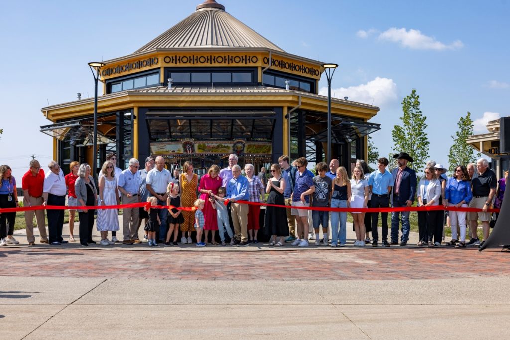 A group of people gathered for a ribbon-cutting ceremony in front of a colorful, ornate gazebo-like structure.