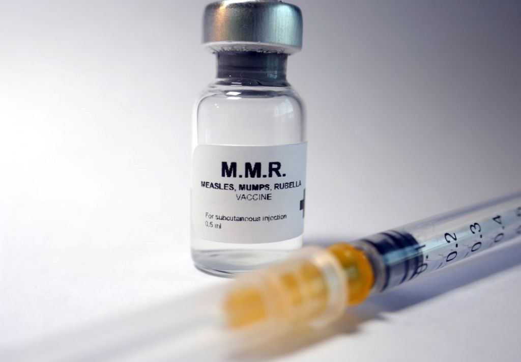 A glass vial labeled "M.M.R. Measles, Mumps, Rubella Vaccine" with a syringe filled with a liquid substance.