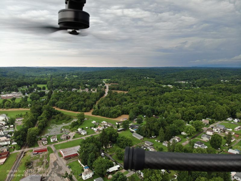 Aerial view of a forested, hilly landscape with a winding road and scattered buildings.